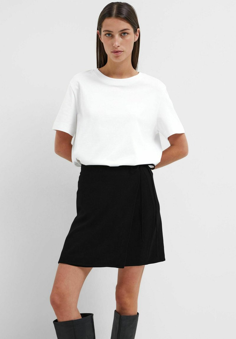 T-shirt bianco a maniche corte abbinato a una gonna nera avvolgente. L'outfit presenta un design minimalistico e una trama di tessuto liscia.