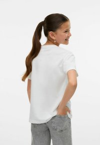 T-shirt blanc à manches courtes, en tissu lisse, coupe décontractée, encolure ronde, associé à un jean taille haute gris clair avec poches arrière.