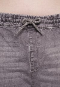 Gros plan sur un pantalon à taille élastique grise avec un nœud de cordon attaché à la taille d'une personne.