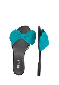Sandale din suede teal cu toc plat, accent cu o fundă mare, talpă neagră și o formă conică. Prezintă o textură netedă și un logo subtil al mărcii.