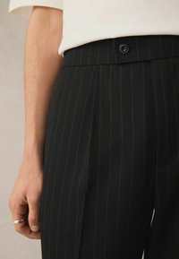 Pantaloni neri a righe sottili realizzati in tessuto intrecciato, con frontale piatto, chiusura con bottone a vista e tasca laterale.