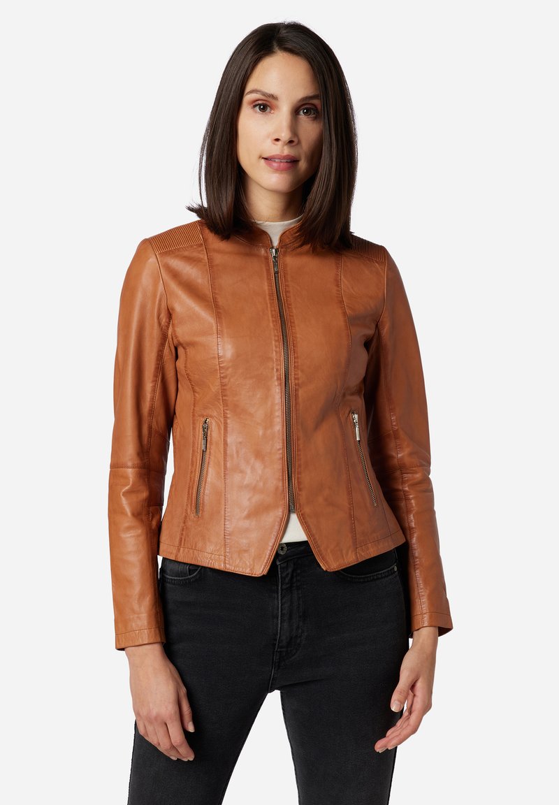Bruine leren jas met een getailleerd ontwerp, rits aan de voorkant, twee zijzakken en een gestructureerde schouderaccenten. Draagt over een lichte top en donkere jeans.