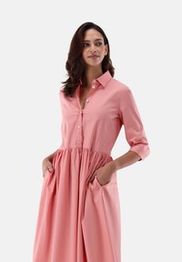 Abito di cotone rosa con colletto, apertura a bottoni sul davanti, maniche a tre quarti, vita elasticizzata e tasche laterali. Tessuto liscio e leggero.