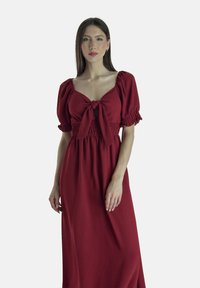 Rotes Maxikleid aus leichtem Stoff. Mit Puffärmeln, gerafftem Taillenbereich und einem vorderen Bindedetail sowie einem tiefen Ausschnitt. Glatte Textur.