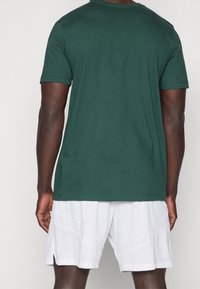 Grøn bomulds T-shirt med korte ærmer, rund halsudskæring og et enkelt design, parret med hvide mesh athletic shorts med geometriske mønstre.