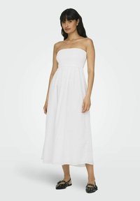 Vestido maxi blanco sin tirantes con cuerpo fruncido y falda fluida. Combinado con zapatos planos negros de punta con tachuelas plateadas.