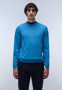 Blauwe gebreide trui met een ronde hals, lange mouwen en geribde manchetten en zoom. Voorzien van een klein logo op de borst. Gecombineerd met donkere broek.