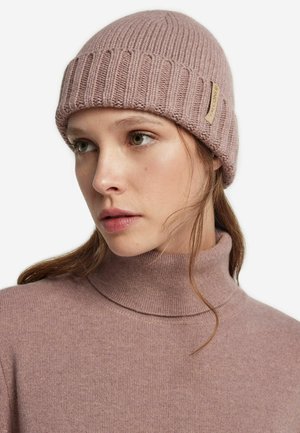 Mjukt rosa stickad mössa med ribbad textur och en liten läderetikett. I kombination med en ljusrosa polotröja.