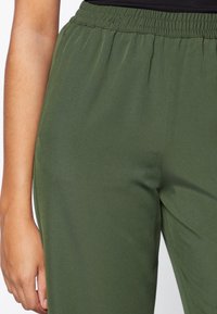 Groene broek met elastische taille van een gladde stof en een losse pasvorm. Kenmerkt zich door een zachte textuur en plooidetails aan de voorkant.