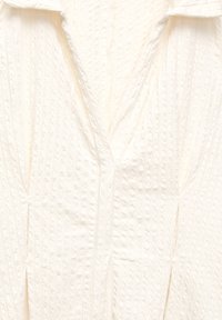 Witte textuurstof met een V-halslijn en subtiele ribbelpatroon, voorzien van een iets gestructureerd kraagontwerp.
