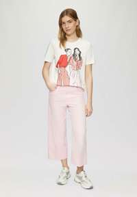 T-shirt blanche avec un motif graphique de deux figures en rouge et des motifs floraux. Pantalon court rose ample et baskets grises. Texture de tissu lisse.