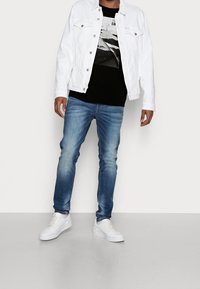 Valkoinen denim-takki, musta graafinen t-paita, vaaleansiniset farkut ja valkoiset lenkkarit. Ominaisuuksiin kuuluu napit, taskut ja slim fit -leikkaus.