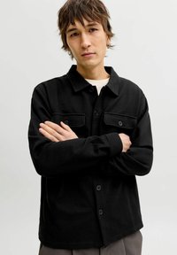 Czarna koszula na guziki z dwoma przednimi kieszeniami, wykonana z teksturowanej tkaniny. Posiada kołnierzyk i długie rękawy, zaprojektowana o luźnym kroju.