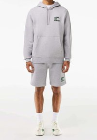 Sweat-shirt gris avec capuche et poche avant, associé à un short gris assorti. Les deux présentent "GAME, SET, MATCH!" en texte vert. Baskets blanches.