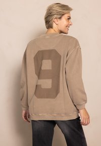 Oversized beige sweatshirt with a large brown number 9 print on the back, featuring ribbed cuffs and a crew neck design.