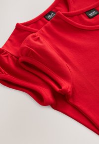 Red cotton t-shirts with round necks and gathered short sleeves, displaying smooth texture and clean stitching. Labels are visible inside.