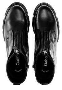 Bottes noires en cuir au-dessus de la cheville avec une texture lisse, fermetures éclair sur le côté et semelle en caoutchouc. L'intérieur présente un logo et un soutien rembourré.