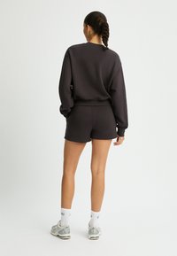 Set di felpa e pantaloni corti grigi scuri realizzato in un tessuto morbido. La felpa ha maniche lunghe e polsini a costine; i pantaloni corti sono aderenti con una vita elasticizzata.