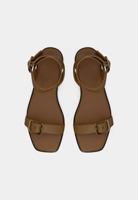 Καφέ επίπεδα σανδάλια με τετράγωνη μύτη, με έναν ιμάντα και αγκράφα σε χρυσή απόχρωση, και λείο υφή πέλματος.