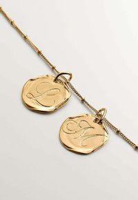 Collar de cadena de oro que presenta dos charms colgantes texturizados con las letras en relieve "L" y "M". Acabado suave y brillante con detalles intrincados.