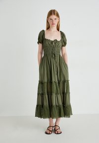 Olijfgroen jurk met korte pofmouwen, vierkante halslijn en smock-bodice. Bevat kantafwerking en een gelaagde rok met doorschijnende kantsecties.