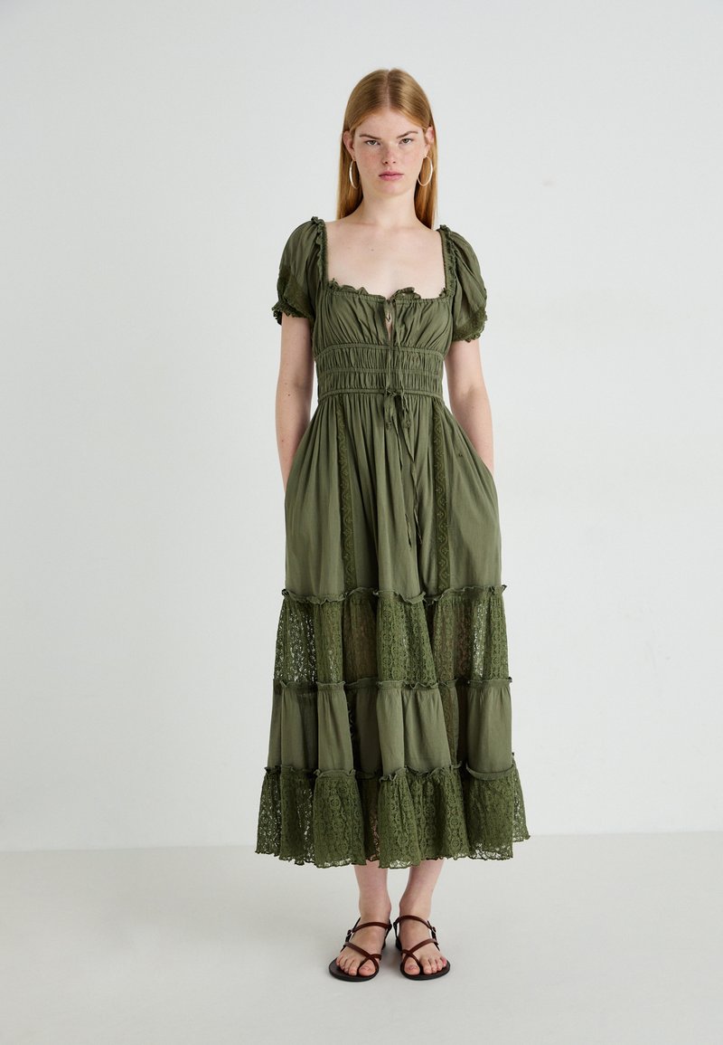 Olijfgroen jurk met korte pofmouwen, vierkante halslijn en smock-bodice. Bevat kantafwerking en een gelaagde rok met doorschijnende kantsecties.