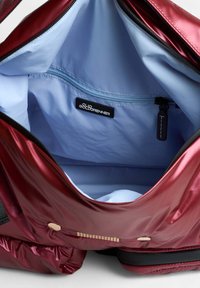Bordeaux rugzak met een glanzende textuur en een gladde stof. Lichtblauwe binnenkant, voorzien van een ritszak en een zwart label aan de binnenkant. Gouden accenten.