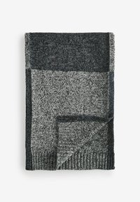 Stickad filt med en texturerad yta, med en design i mörkgrå och ljusgrå färgblock. Avslutad med en ribbad kant.