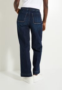 Jean en denim bleu foncé avec une coupe décontractée, des poches arrière brodées et une conception à jambe droite avec un bas légèrement plus large à la cheville.