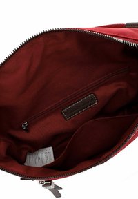 Intérieur d'un sac en tissu rouge avec une poche zippée, texture lisse et une étiquette en cuir. La doublure a une teinte foncée complémentaire.