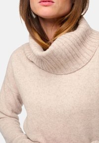 Helle beige Strickjacke mit einem gerippten Kragen und weicher Textur, die einen entspannten Schnitt und subtile Steppdetails aufweist.