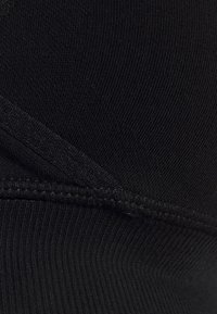 Μαύρο ελαστικό ύφασμα με ραφές, διαθέτοντας καμπυλωτές ραφές και επίπεδη ραφή κατά μήκος των άκρων.