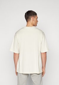 Grau-weißes, oversized T-Shirt mit kurzen Ärmeln, aus weicher Baumwolle. Mit Rundhalsausschnitt und schlichtem, klaren Design.