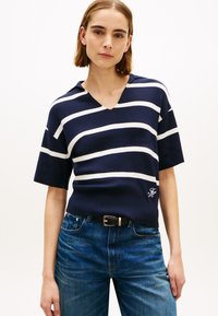 Κοντομάνικη μπλούζα με ριγέ σκούρο μπλε και λευκό, με V-λαιμόκοψη, κατασκευασμένη από μαλακό πλεκτό ύφασμα, με κεντημένο λογότυπο στο στρίφωμα.