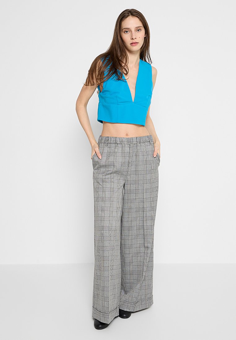 Blauwe crop top met een diepe V-hals, gecombineerd met hooggetailleerde, wijde grijze geruite broek. Bevat zakken en een geruit patroon.