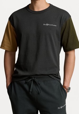 T-shirt noir à manches courtes avec des manches vertes et brunes ; présente une impression de logo sur la poitrine. Associé à un pantalon de jogging noir à cordon.