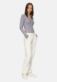 Lichtpaarse geribde lange mouw top gecombineerd met witte cargobroek. De broek heeft zijzakken. Het model draagt beige platform sneakers.