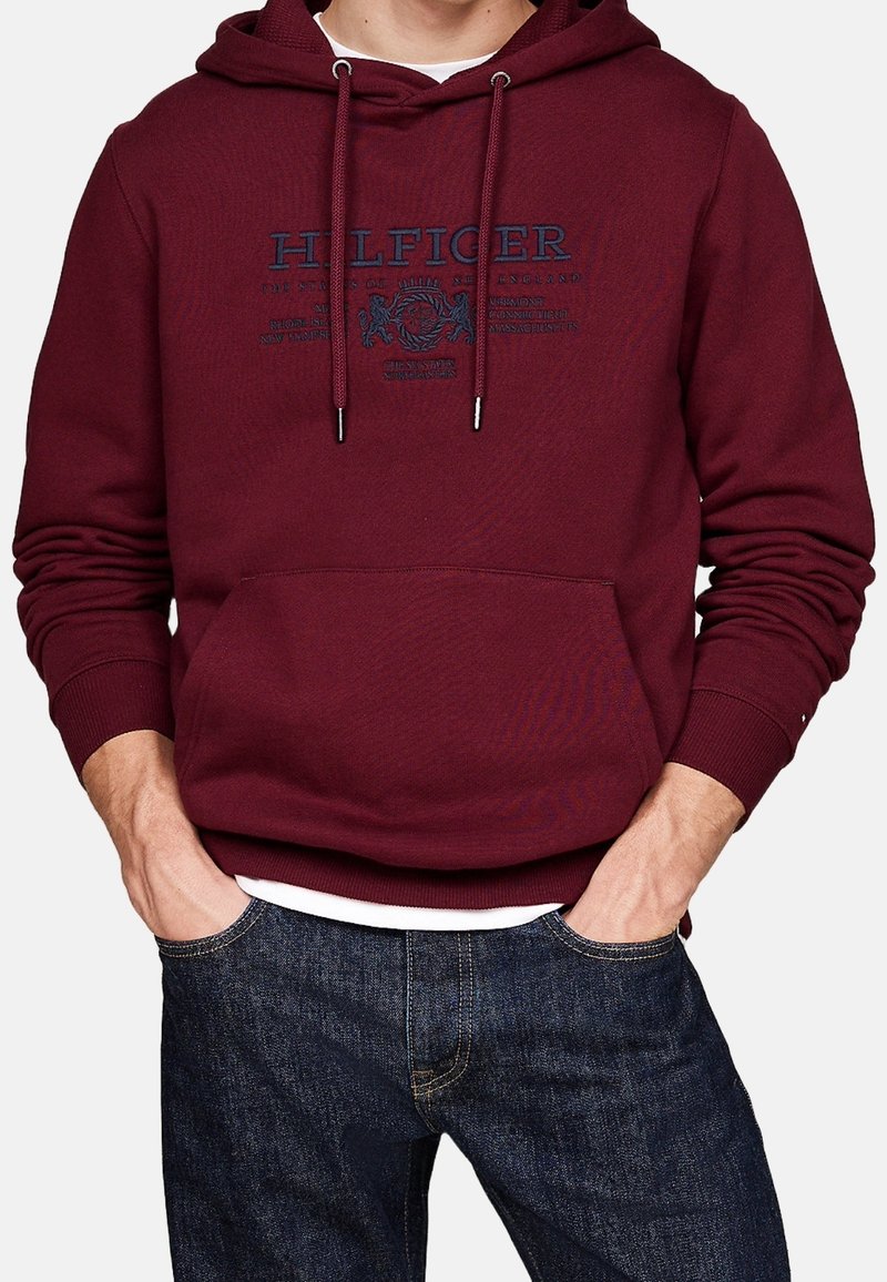 Bordeaux hoodie med känguruficka, dragsko på huvan och tryckt logo i marinblått. Tillverkad i bomull med ribbad manschett och nederkant. Enkelt design.