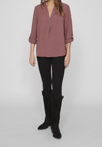 Chemise couleur marsala avec un col en V et des manches trois-quarts, associée à un pantalon skinny noir et des bottes hautes en daim noir.