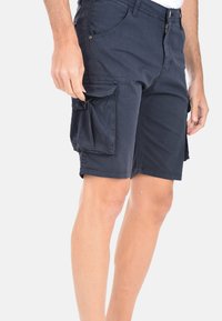 Pantaloni cargo navy realizzati in tessuto misto cotone, con due tasche laterali, zip e adattamento rilassato. Superficie leggermente testurizzata.