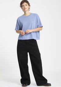 Maglietta in cotone blu a maniche corte, accorciata, abbinata a pantaloni neri larghi. Design semplice senza motivi o dettagli visibili.