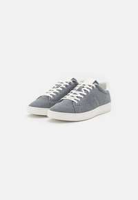 Un paio di sneaker casual a basso profilo con tomaia in tessuto grigio, lacci bianchi e suole in gomma bianca su uno sfondo bianco uniforme.