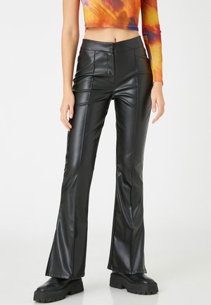 Pantalones acampanados de imitación piel negra con textura suave, detalles de costura en la parte frontal y cinturilla alta, combinados con botas negras gruesas.