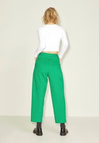 Vit långärmad crop top i kombination med högmidjade, vida gröna byxor och svarta kraftiga skor. Slät tyg utan synliga mönster.