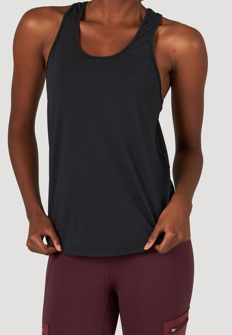 Femme portant un débardeur noir sans manches et des leggings bordeaux taille haute avec poches latérales, les mains tenant l'ourlet du débardeur.