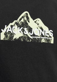 Czarna bawełniana koszulka z grafiką gór w jasnym zielonym kolorze, z napisem "JACK & JONES" i podniszczonym wzorem poniżej.