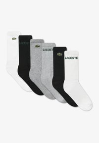 Five pairs of socks in white, black, grey, featuring ribbed texture and green Lacoste logos, with "LACOSTE" text on select pairs.