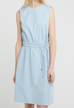 Robe sans manches bleu clair mi-longue, avec un col rond et une taille cintrée à cordon, portée par une personne debout aux cheveux blonds.