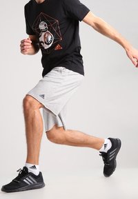 Camiseta negra con un diseño gráfico, pantalones cortos grises, zapatillas negras con rayas blancas y calcetines blancos. Enfóquese en ropa activa para mayor comodidad.