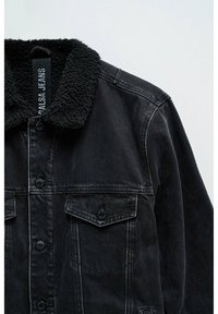 Chaqueta de mezclilla negra con un cuello forrado de sherpa, cierre frontal de botones y dos bolsillos en el pecho. Textura sutilmente desgastada y detalles de costura en contraste.